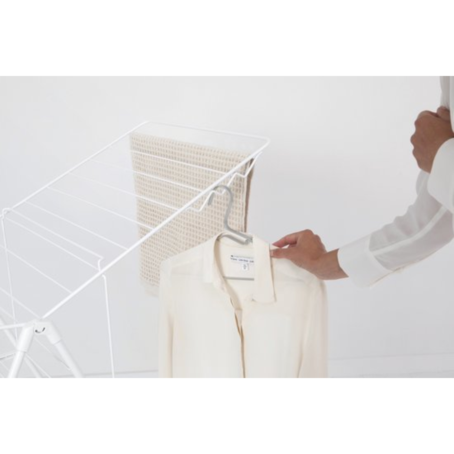 A person hangs a shirt on a hanger, near a drying rack with a towel.
