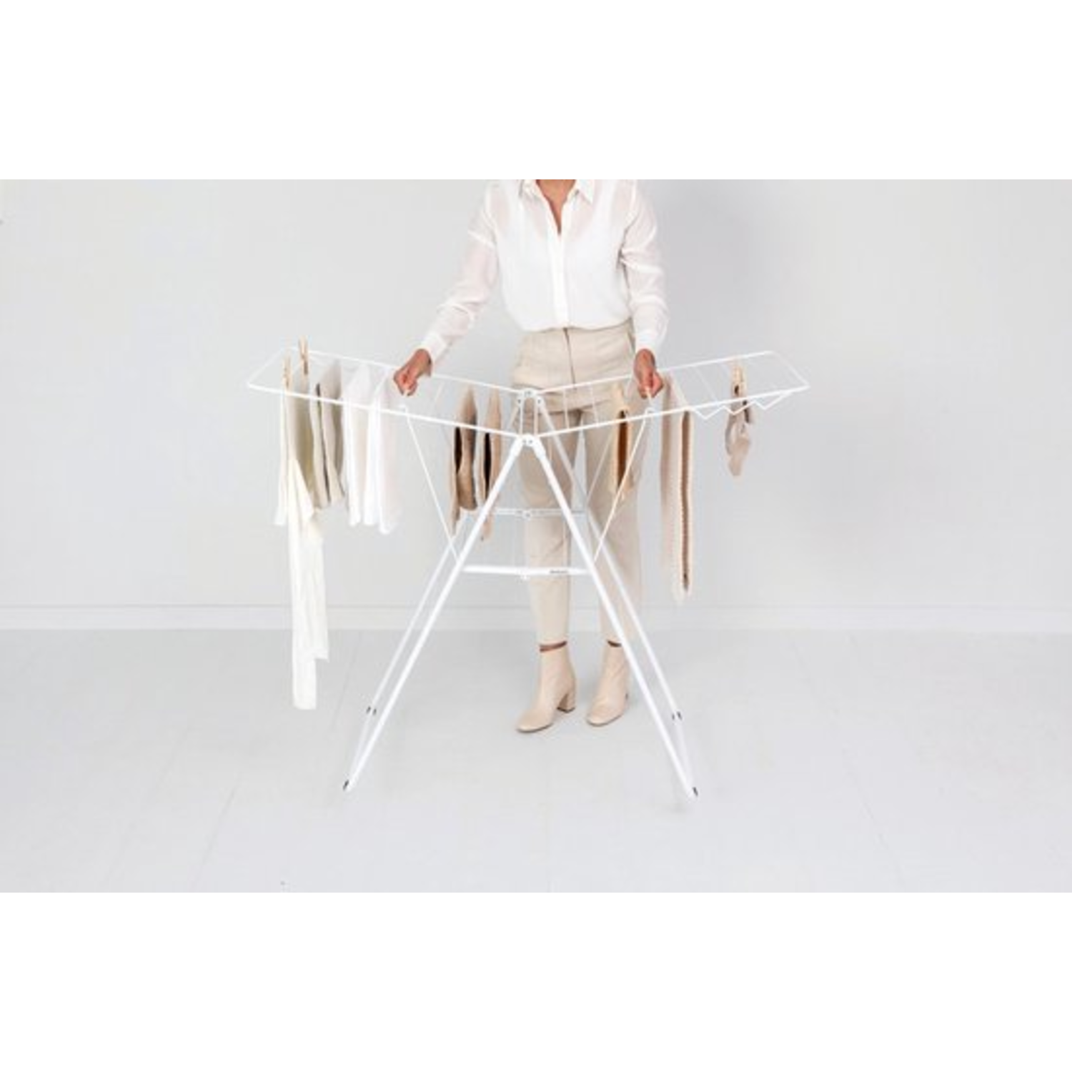 A woman stands by the white drying rack, hanging clothes on it.