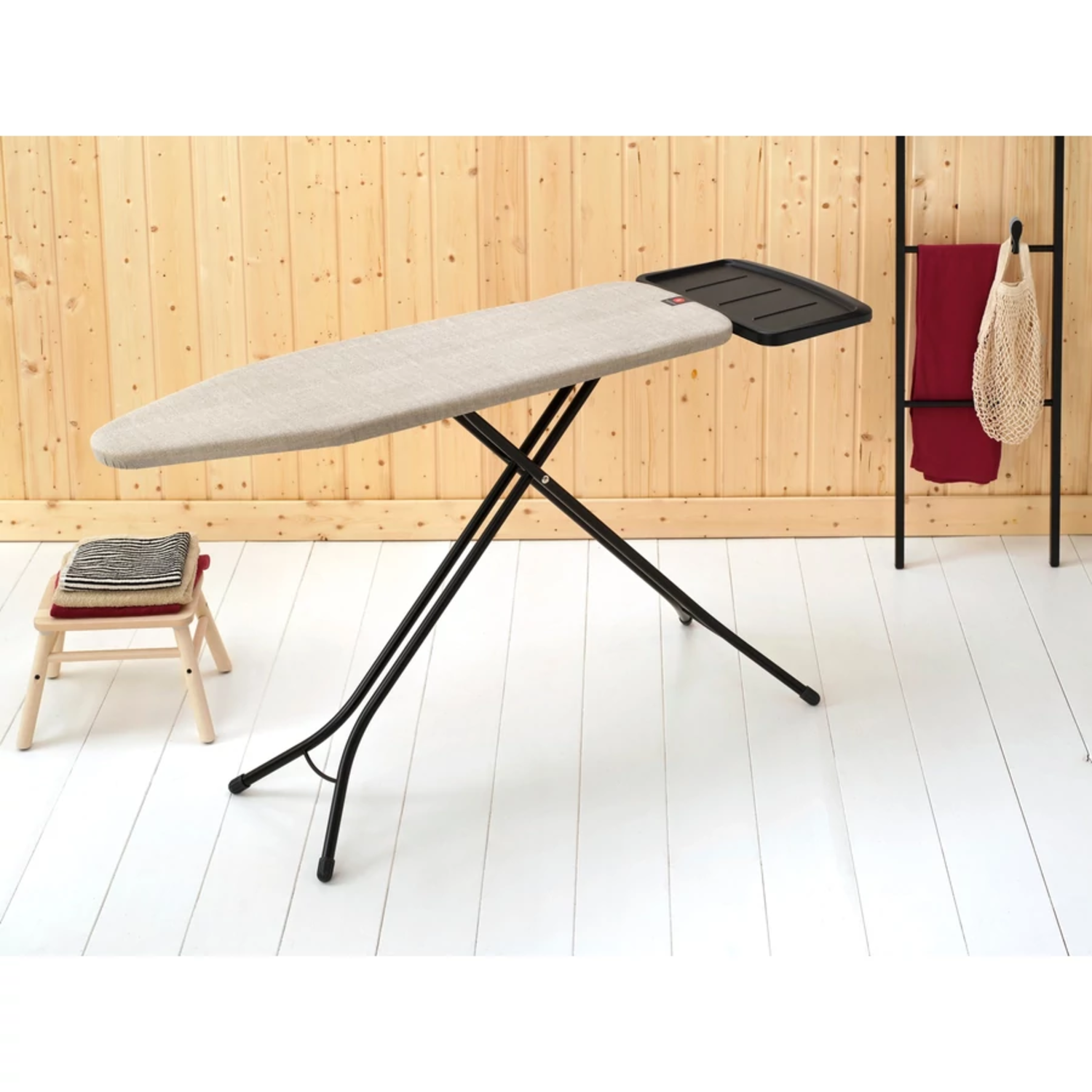 Table à repasser avec pieds noirs et surface beige, dans une pièce aux murs en bois.