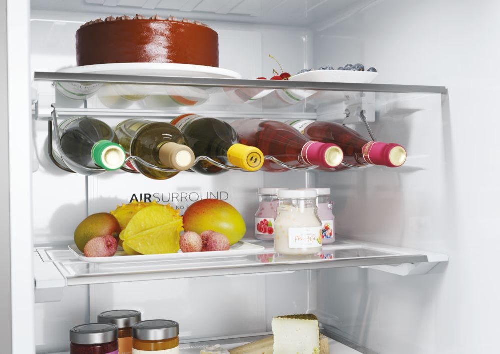 Innenraum des Kühlschranks mit Kuchen, Weinflaschen, Obst und Gläsern mit Lebensmitteln auf Regalen. AirSurround-Etikett sichtbar.