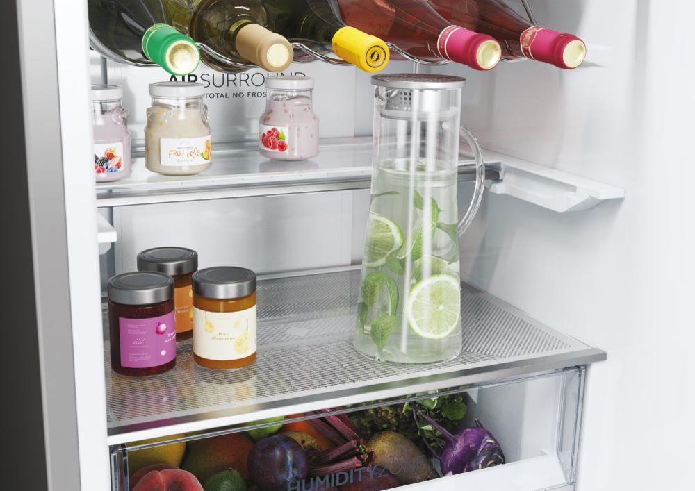 Kühlschrankinnenraum mit Gläsern, einem Wasserkrug mit Limette und Obst. Weinflaschen sind oben sichtbar.