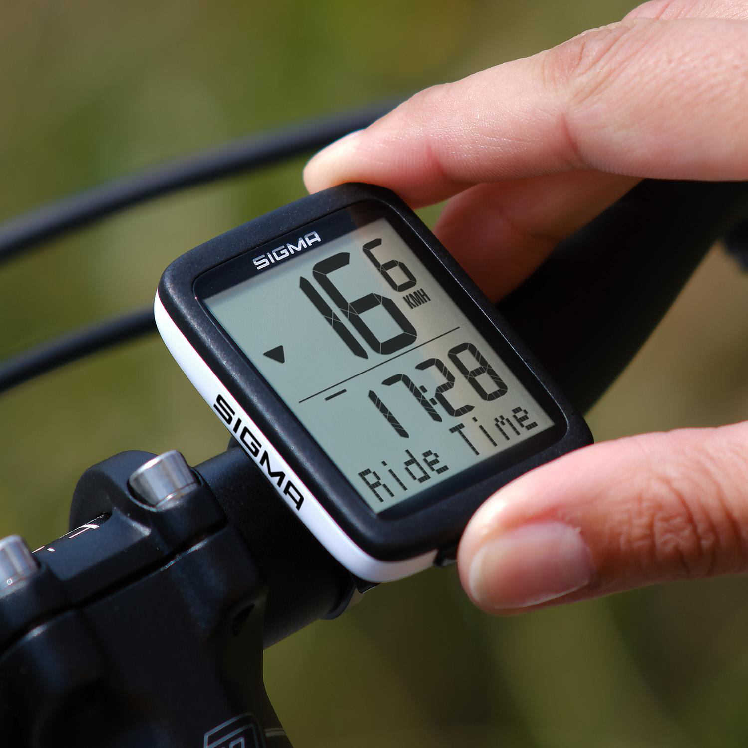 Die Hand eines Radfahrers stellt einen Fahrradcomputer ein, der Geschwindigkeit und Zeit anzeigt. Der Bildschirm zeigt 16 km/h und 17:28.