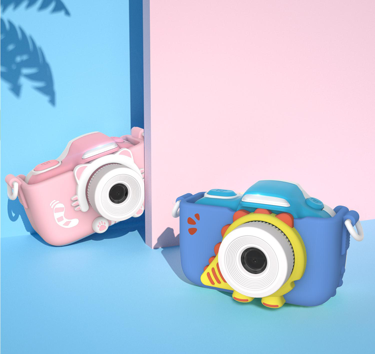 Zwei Spielzeugkameras auf einem rosa und blauen Hintergrund. Eine ist rosa mit einem Katzengesicht. Die andere ist blau mit einem Dinosauriergesicht.