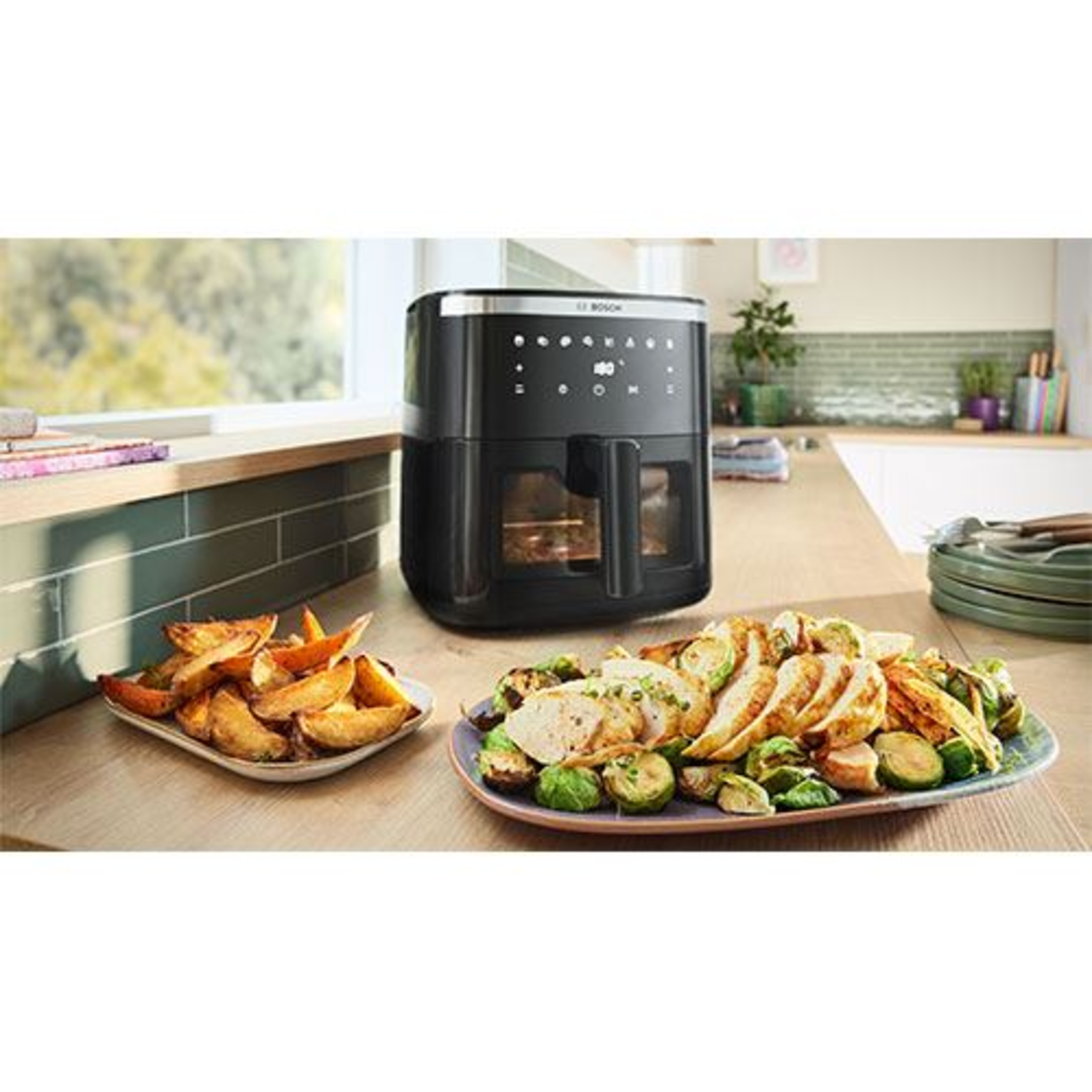 Une friteuse à air Bosch avec des assiettes de nourriture. Des pommes de terre frites et de la viande sont présentées sur des assiettes.
