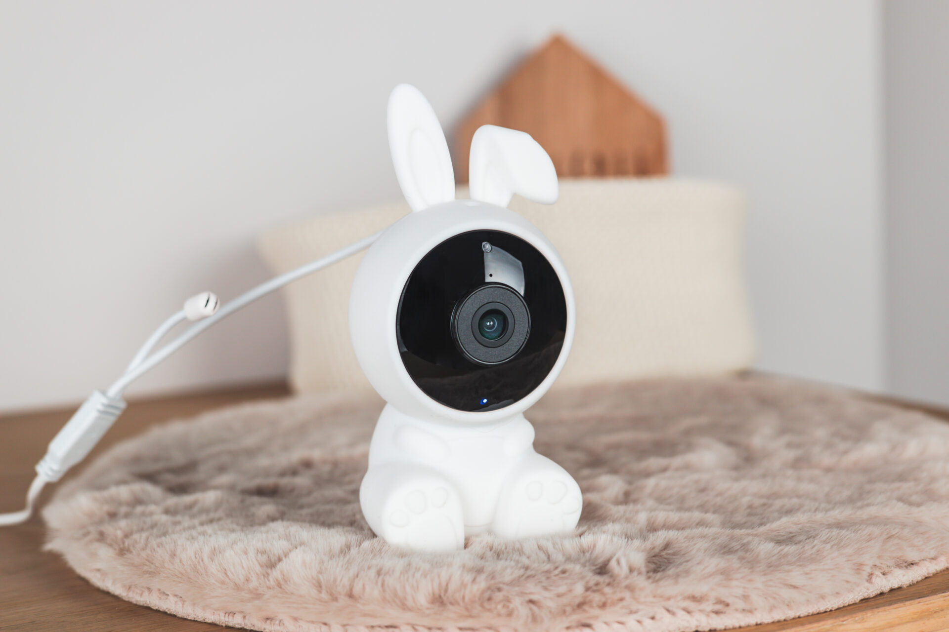 Biały monitor dziecięcy w kształcie królika na puszystym dywanie. Mała dekoracja domu i poduszka w tle.