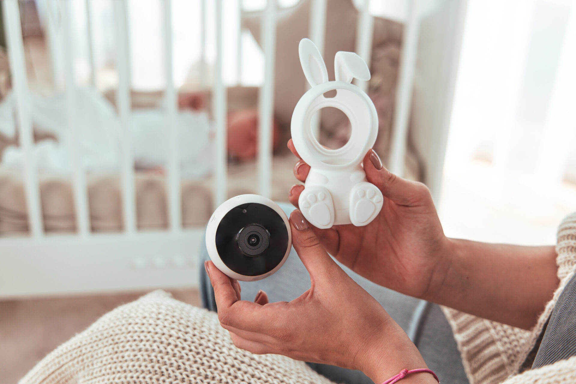 Ręce trzymające części monitora dziecięcego w kształcie królika. Dziecko jest w łóżeczku w tle.