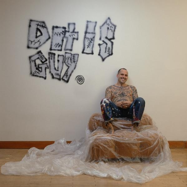 Photo d'un homme assis sur une chaise, avec des graffitis sur un mur derrière lui.