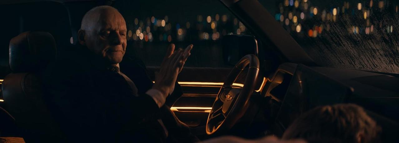 Anthony Hopkins in einem Auto, gestikulierend. Stadtlichter und ein verschwommener Hintergrund sind sichtbar.