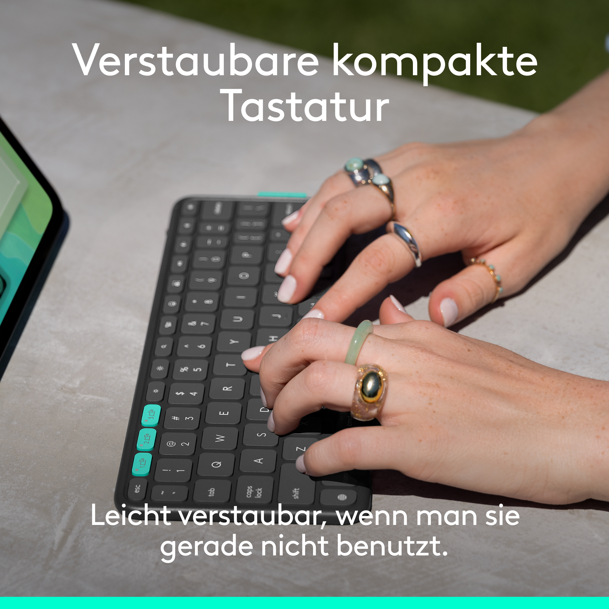 Hände mit Ringen tippen auf einer Tastatur. Die Tastatur hat teal Akzente.