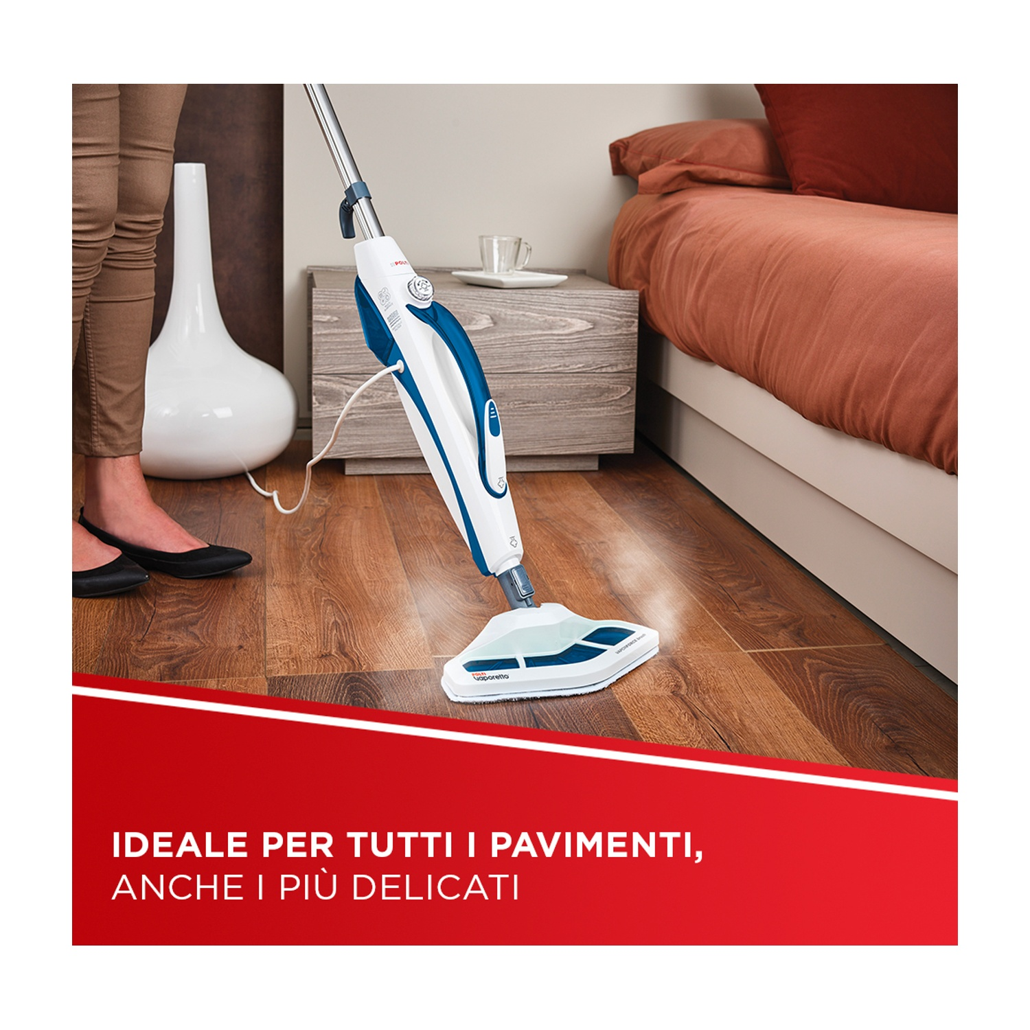 Una persona usa un pulitore a vapore su un pavimento in legno. Un letto e un vaso sullo sfondo.