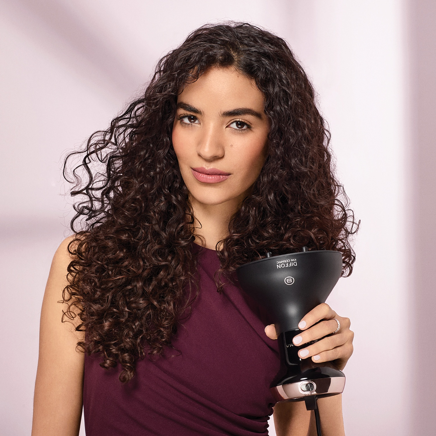 Donna con capelli ricci che tiene un diffusore nero. Indossa un vestito bordeaux.