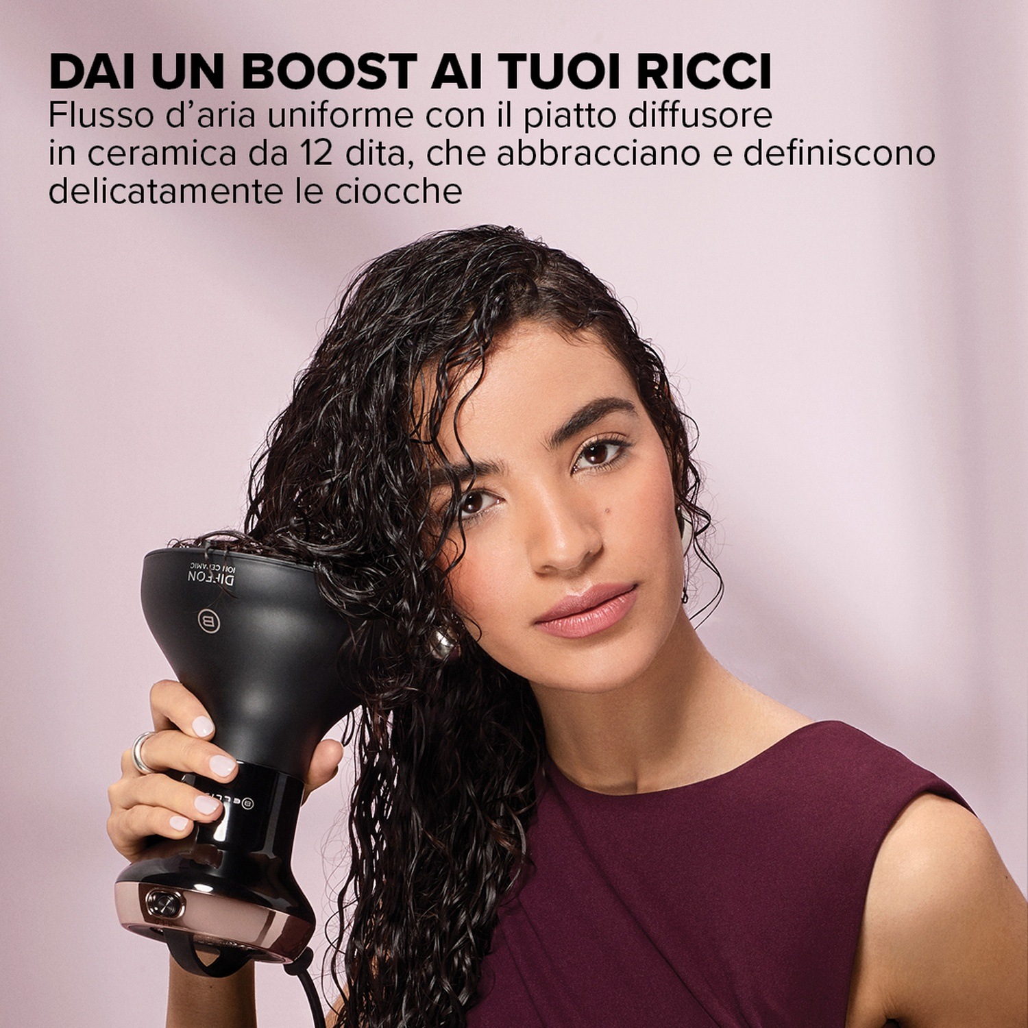 Donna usa un diffusore sui suoi capelli ricci. Il prodotto promuove ricci definiti. Vestito bordeaux.