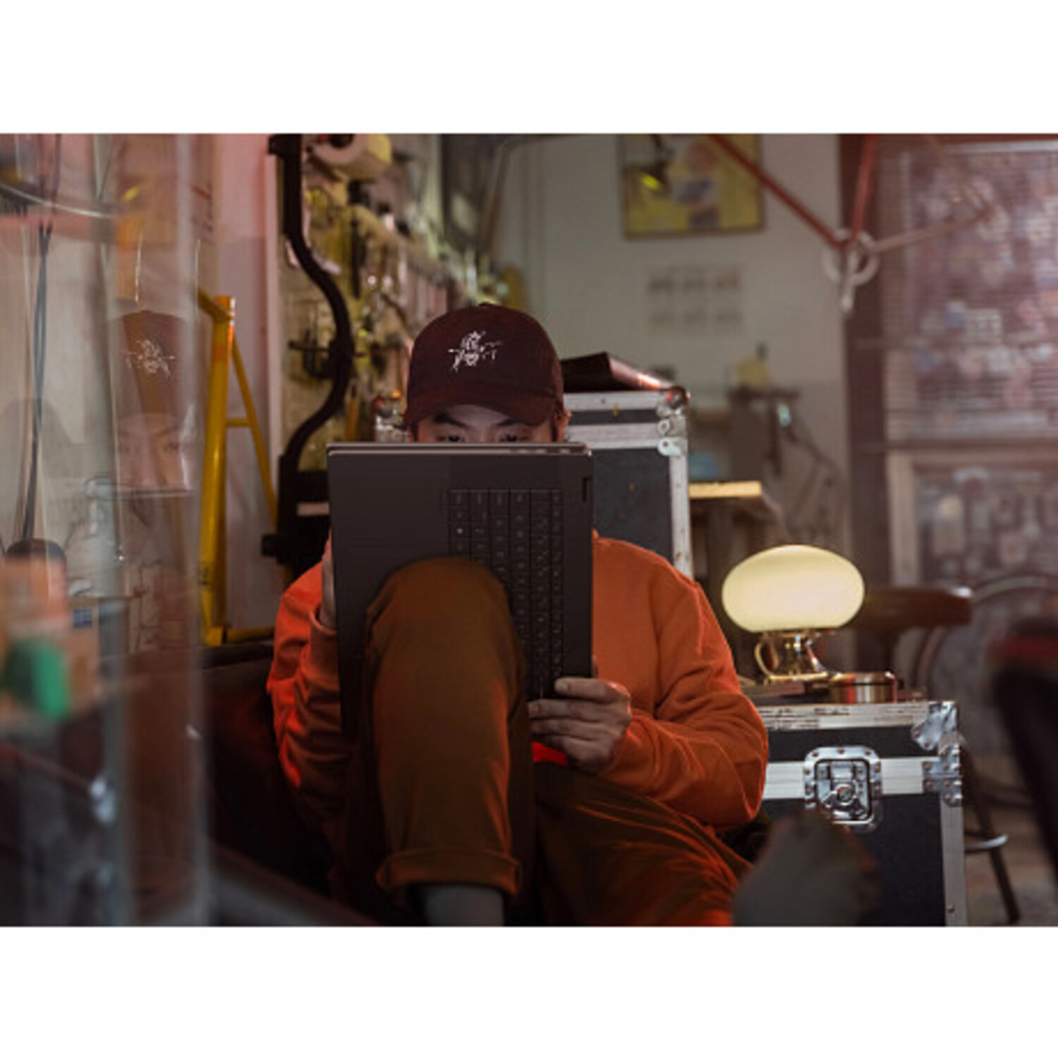 Homme portant une casquette utilisant un ordinateur portable dans un atelier faiblement éclairé. Écran visible.