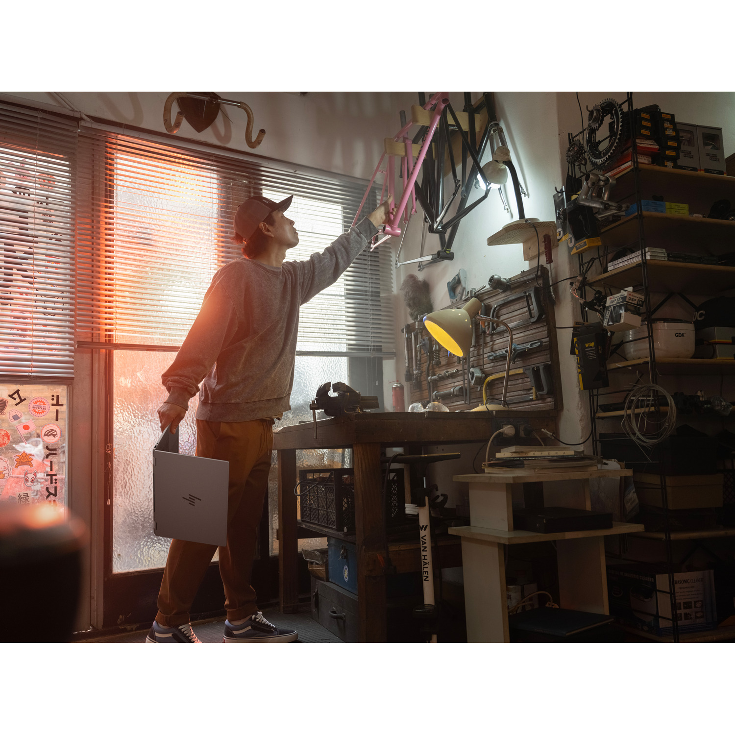 Homme dans un atelier tendant la main vers un cadre de vélo, tenant un ordinateur portable.