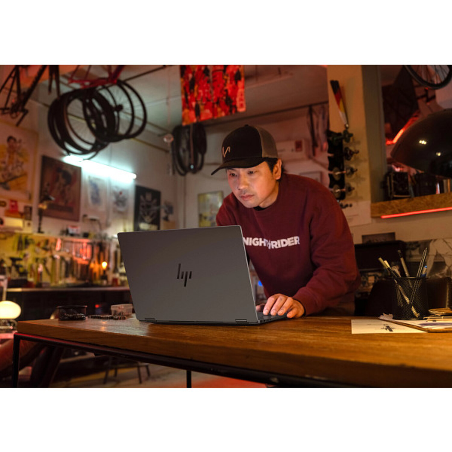 Homme dans un atelier utilisant un ordinateur portable, appuyé sur une table en bois.