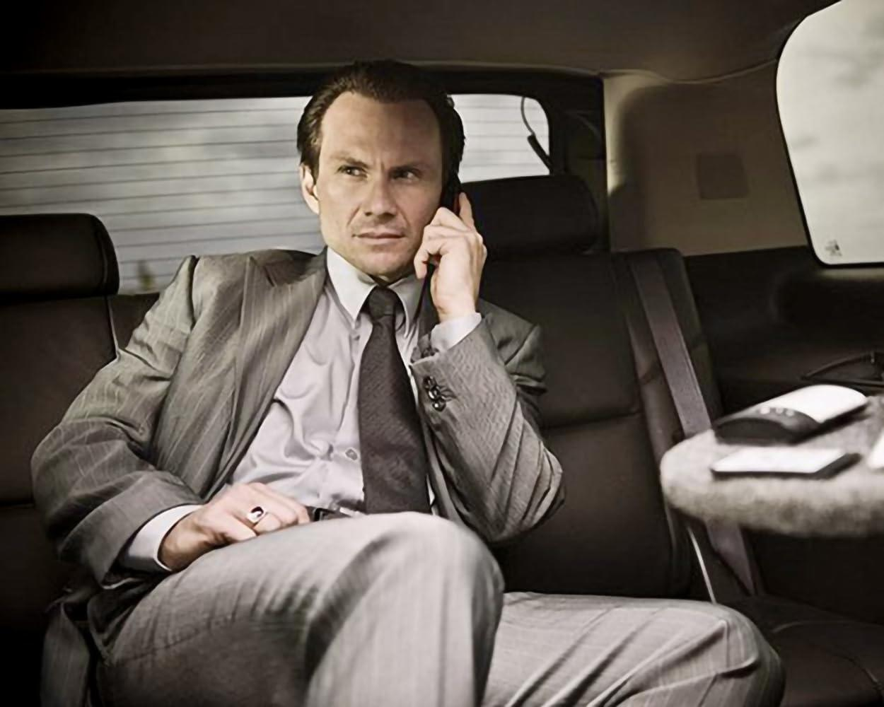 Mann im Anzug sitzt in einem Auto und telefoniert. Innenraum des Autos ist sichtbar.