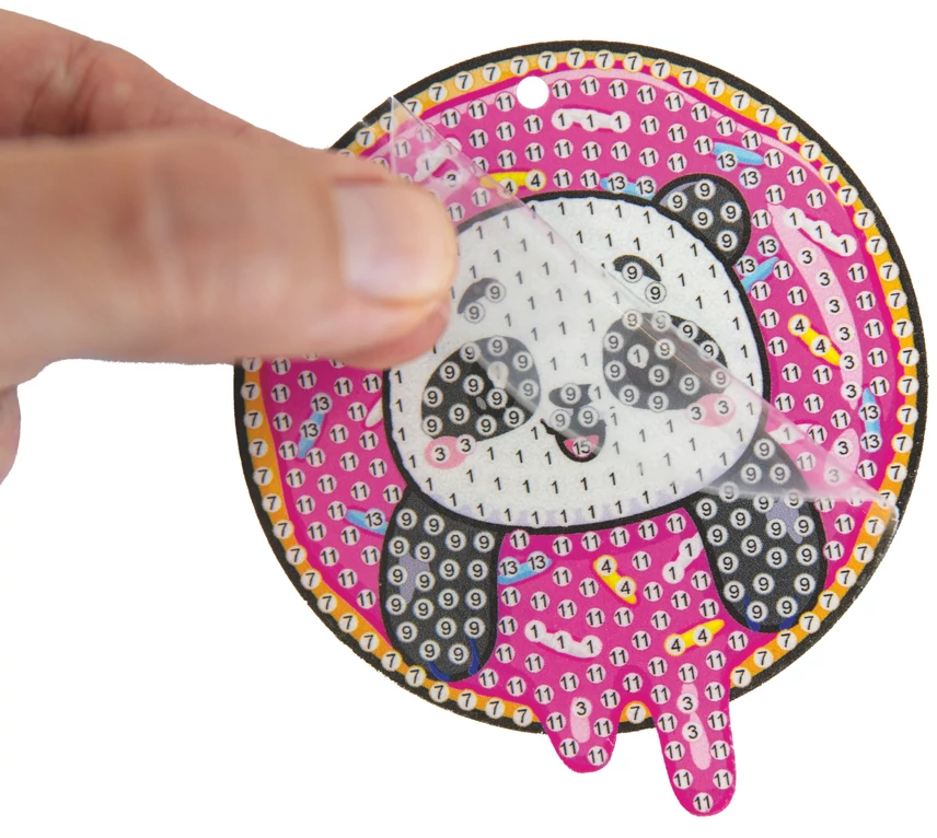 Egy kéz lehúzza a védőfóliát egy panda arc mintáról egy kézműves projekten.