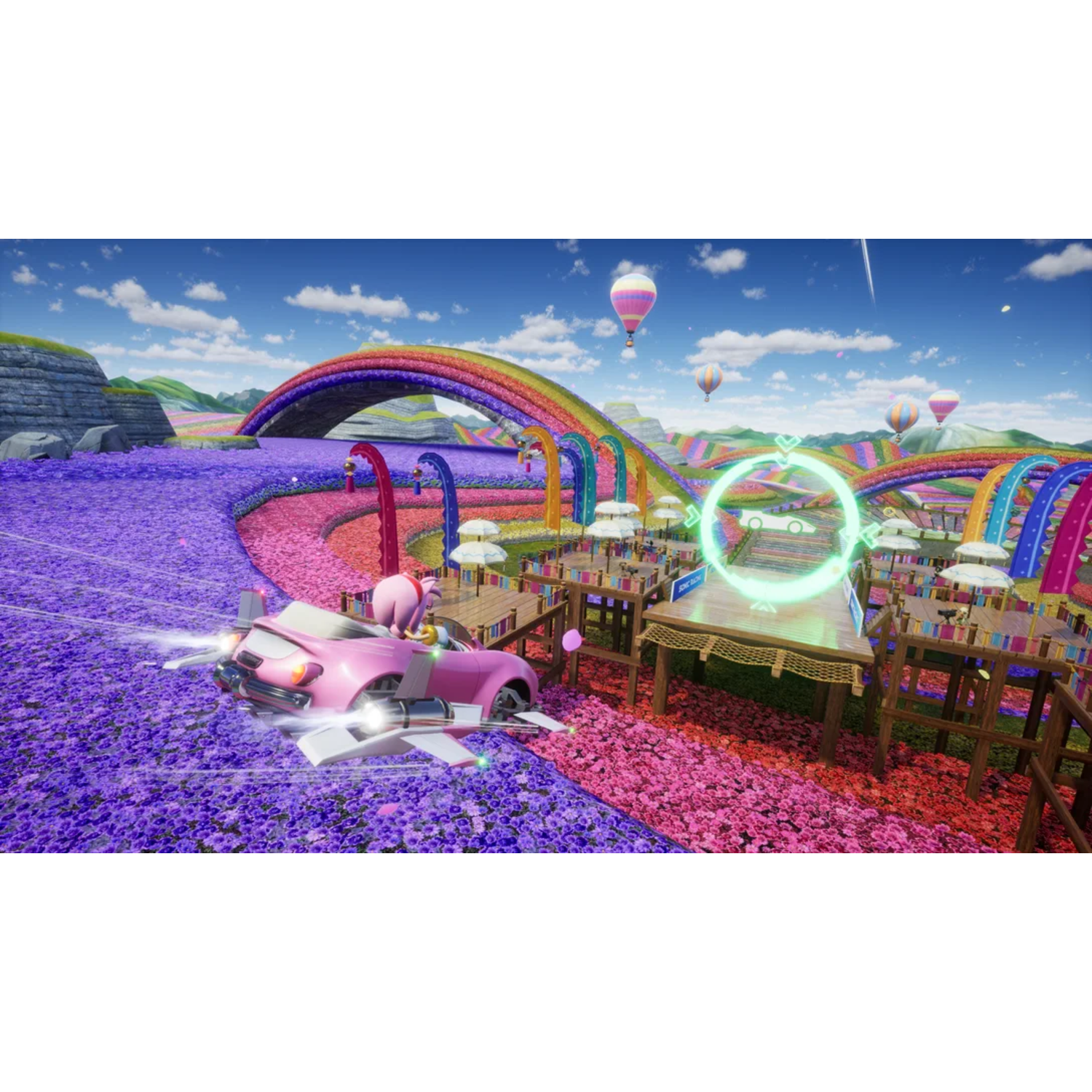 A pink car races on a floral track, with a rainbow and balloons. Tables are set for a picnic.