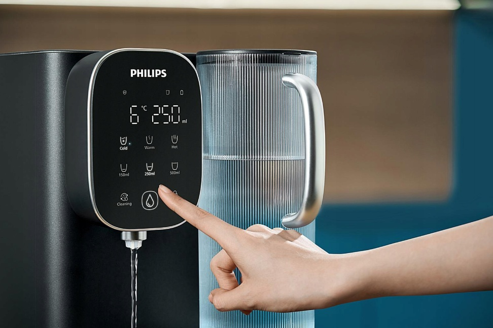 Palec osoby naciska przycisk na czarnym dystrybutorze wody Philips. Zbiornik na wodę jest w tle.