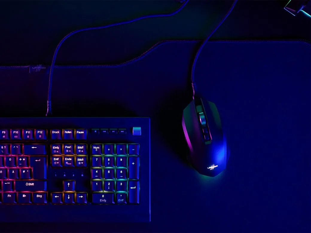 Egy gamer billentyűzet és egér készlet sötét felületen, színes fényekkel megvilágítva. A billentyűzet szivárványos háttérvilágítással rendelkezik.