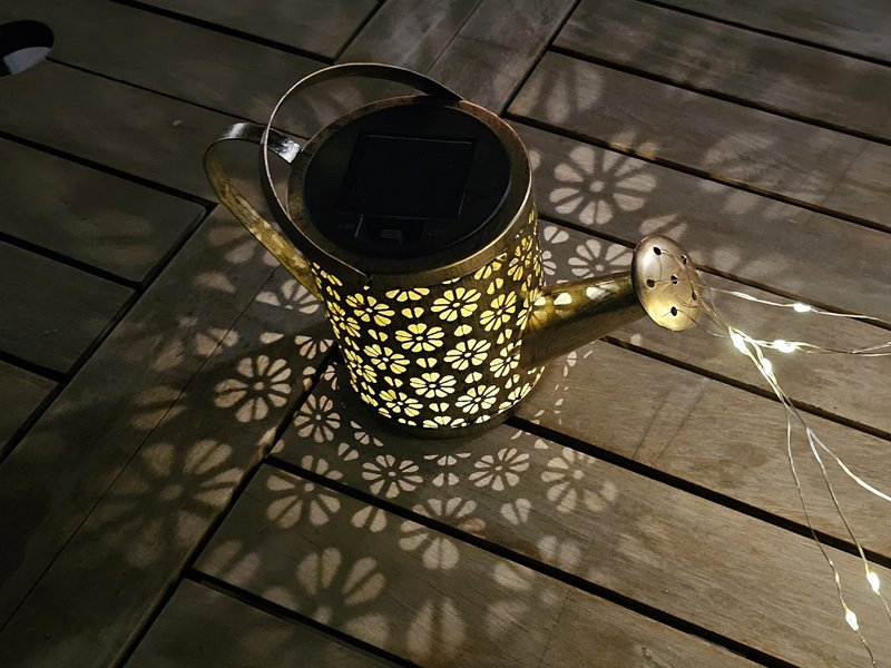 Napenergiával működő öntözőkanna lámpa egy faasztalon.