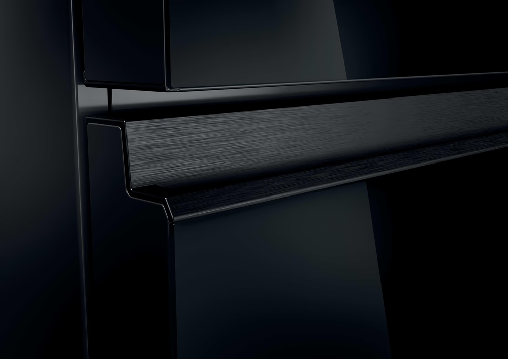 Nahaufnahme eines schwarzen Kühlschrankgriffs und Türausschnitts. Metallisches Finish, glänzende Oberfläche.