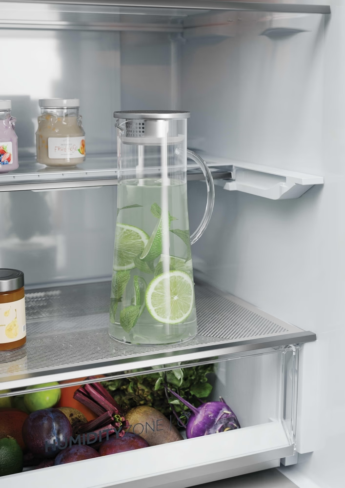 Kühlschrankregal mit Wasserkrug mit Limettenscheiben und anderen Lebensmitteln.