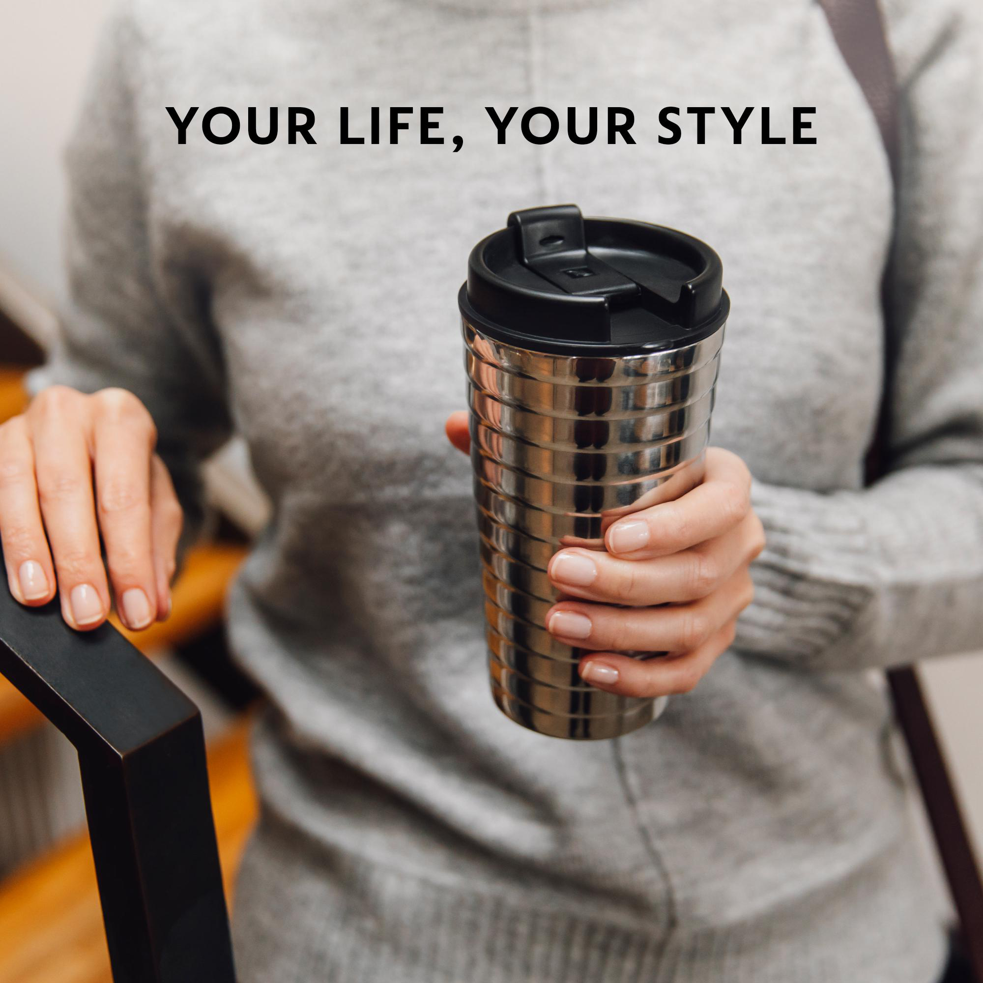Person hält Edelstahl-Nespresso-Becher. Text: Your life, your style. Schwarzer Griff in der Nähe.
