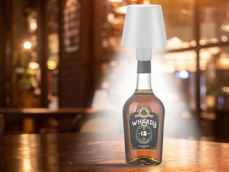 Fehér lámpa egy whisky-palackon, a bárpulton, bokeh háttérrel.