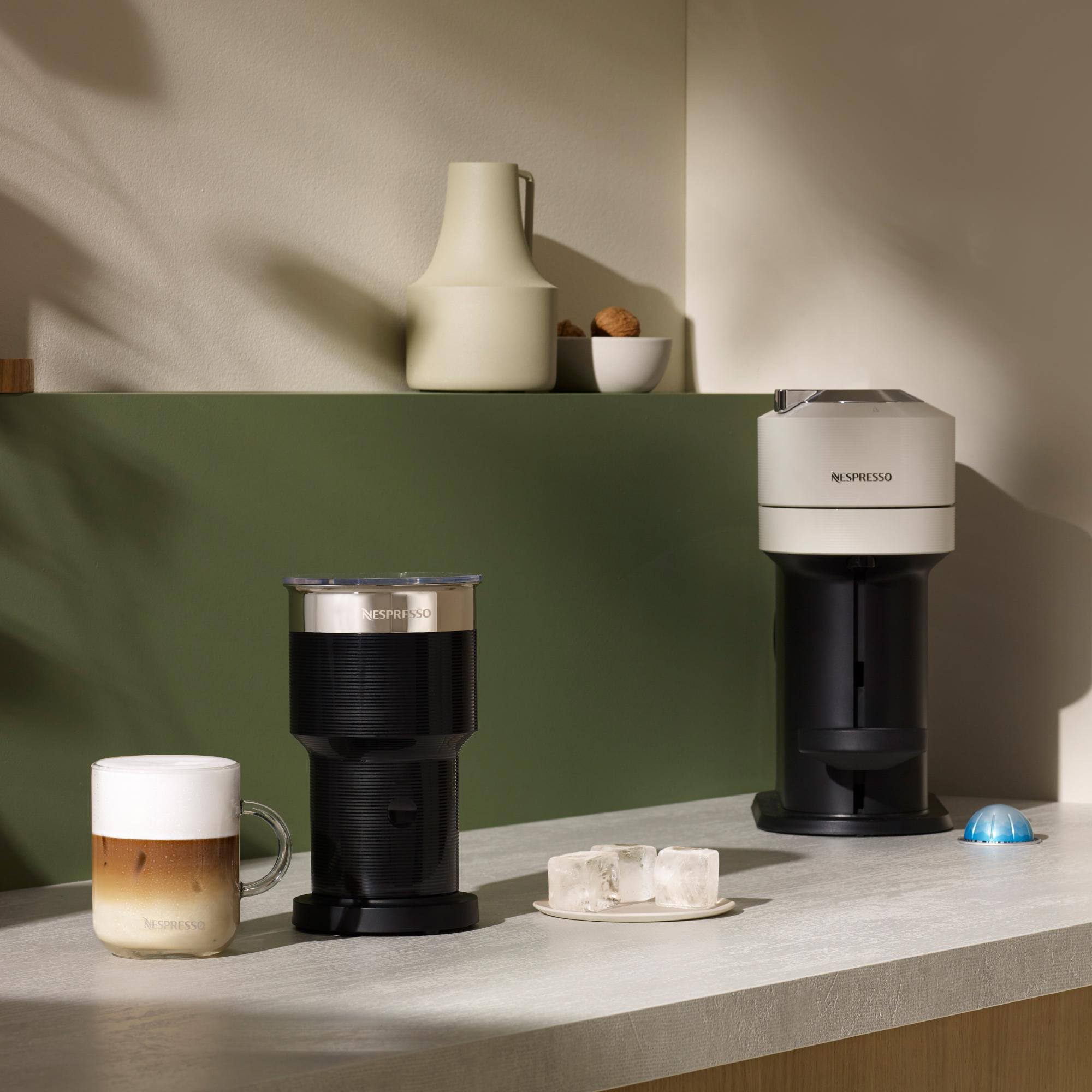 Nespresso-Maschinen, Kaffeegetränk, Eiswürfel und Dekorationsartikel auf einer Arbeitsplatte. Grüner und beiger Hintergrund.