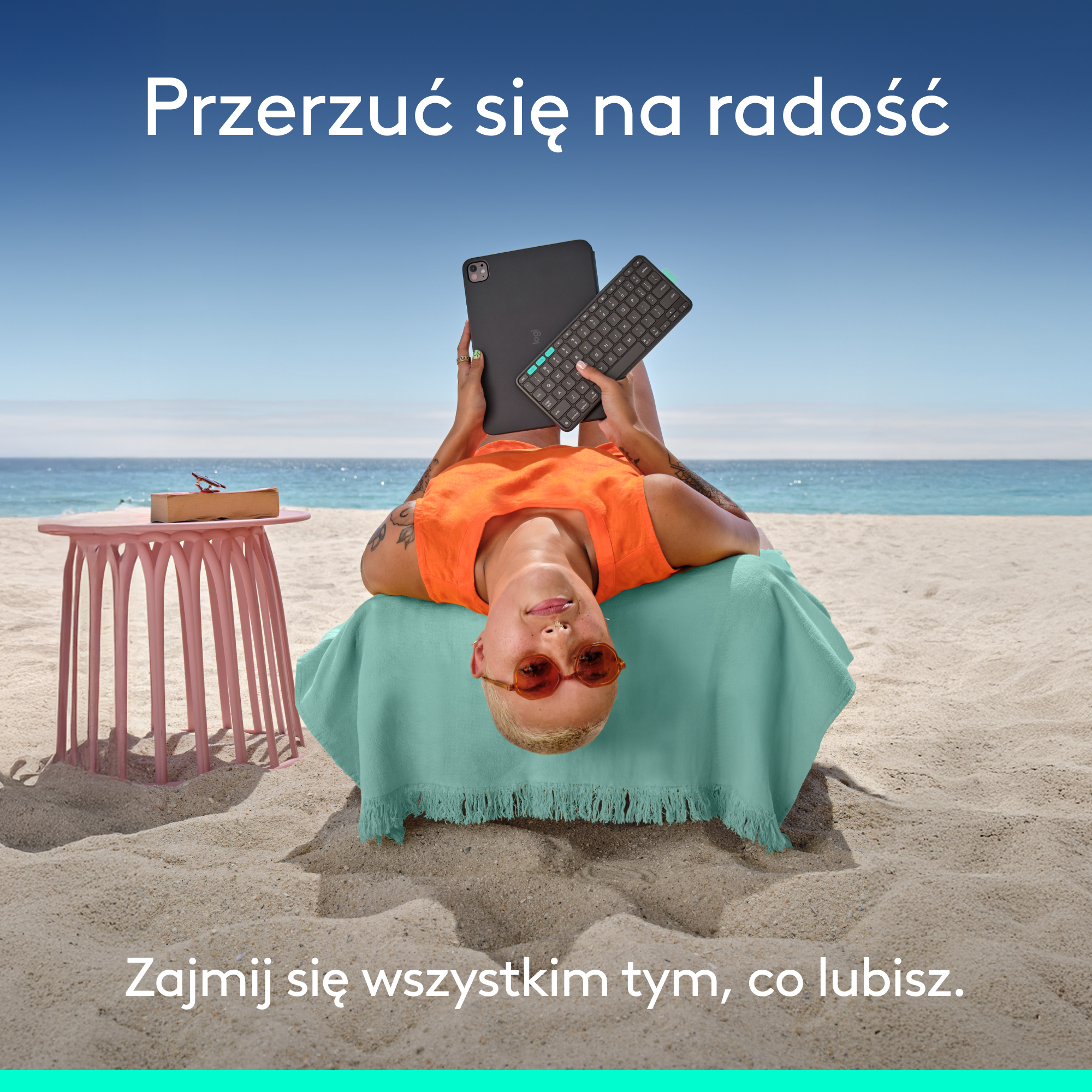 Kobieta leżąca na ręczniku plażowym z iPadem i klawiaturą. U góry tekst 'Switch to joy'.