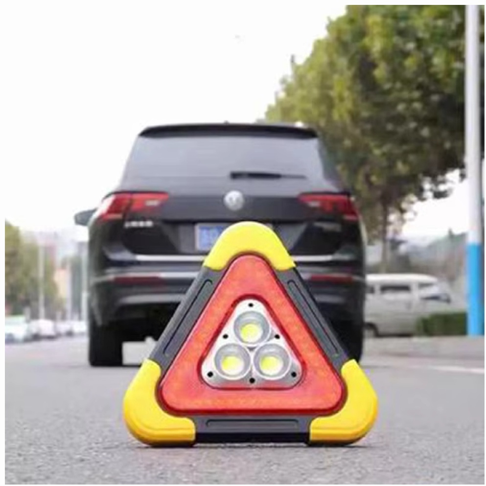 Trójkąt ostrzegawczy na drodze z samochodem w tle.