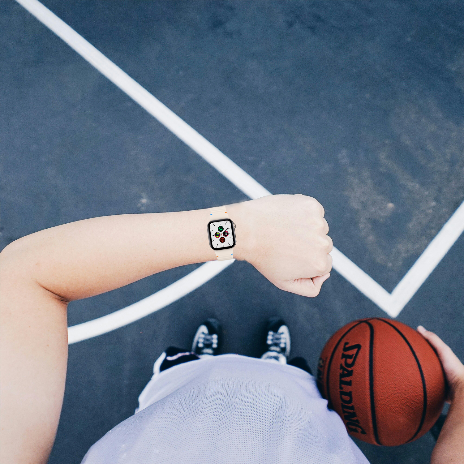 Personne avec smartwatch sur un terrain de basket, tenant un ballon. Vue d'en haut.