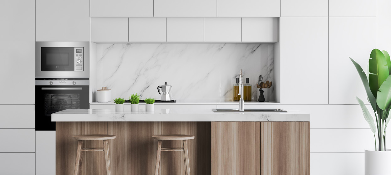Cocina moderna con armarios blancos, encimera de mármol e isla de madera. Incluye microondas, horno y plantas. Dos taburetes en la isla.
