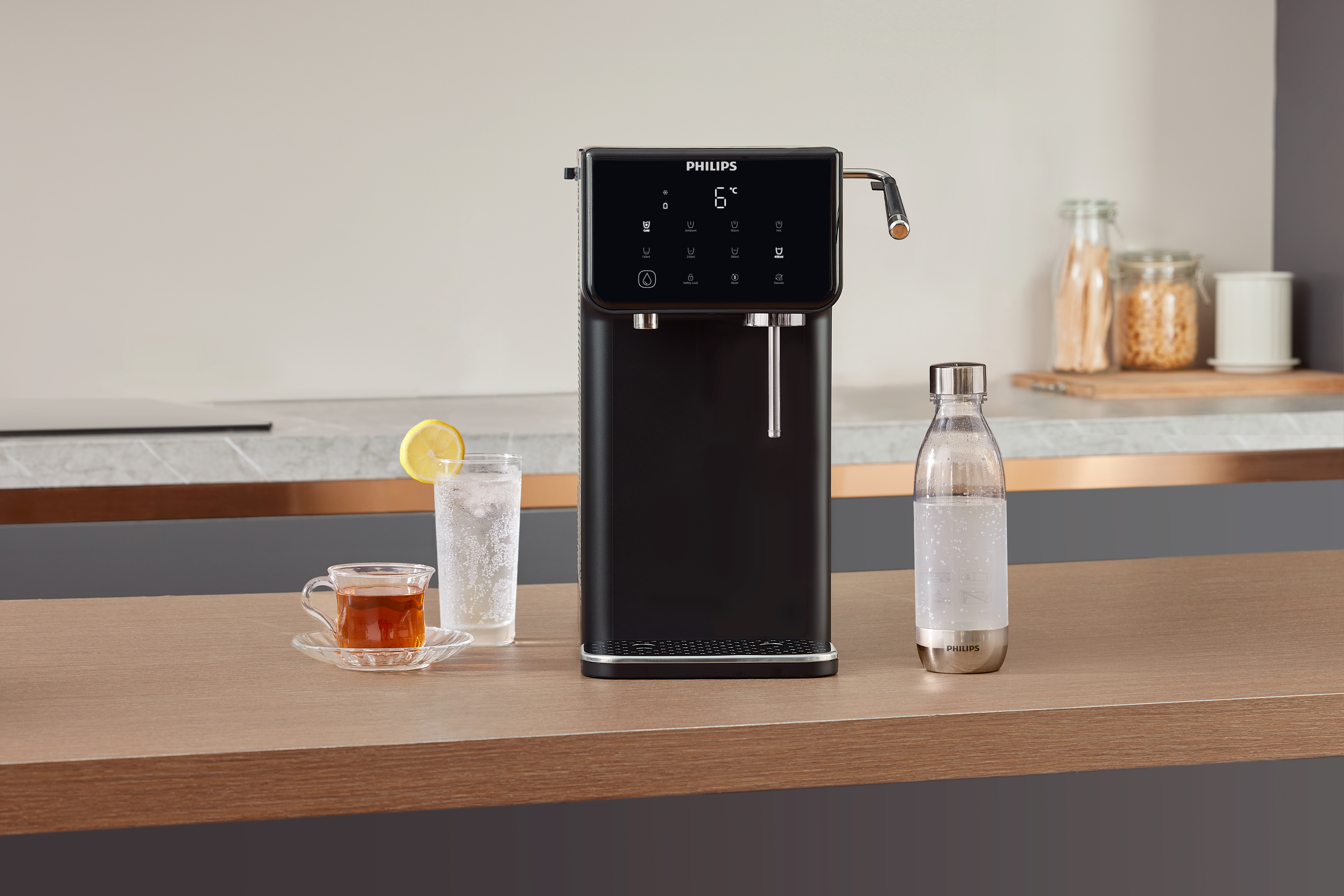 Czarny dystrybutor wody Philips na blacie, ze szklanką i filiżanką herbaty.