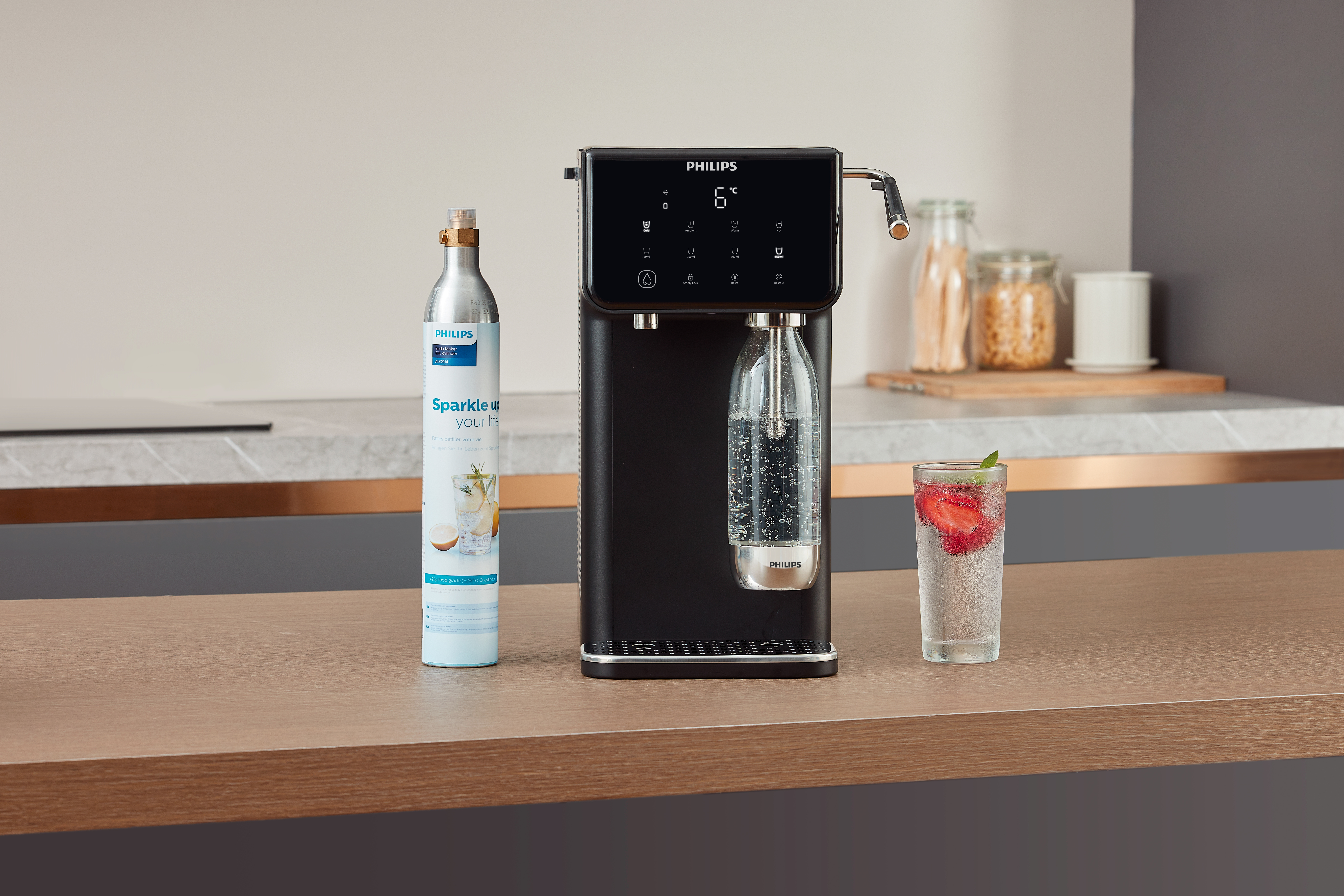 Dystrybutor wody Philips, butelka i szklanka z truskawkami na blacie.