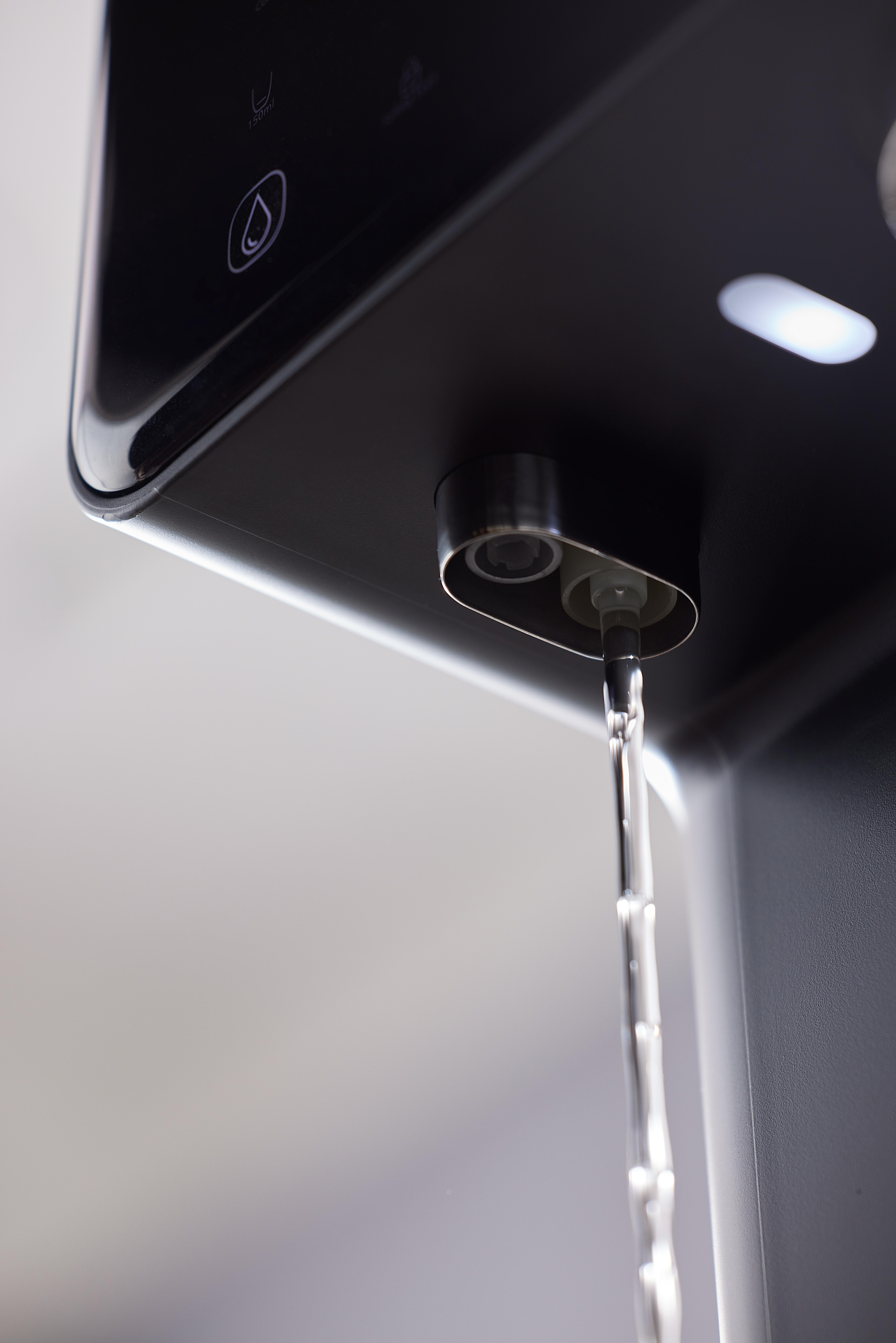 Woda wylewa się z czarnego dystrybutora Philips, widok z bliska.