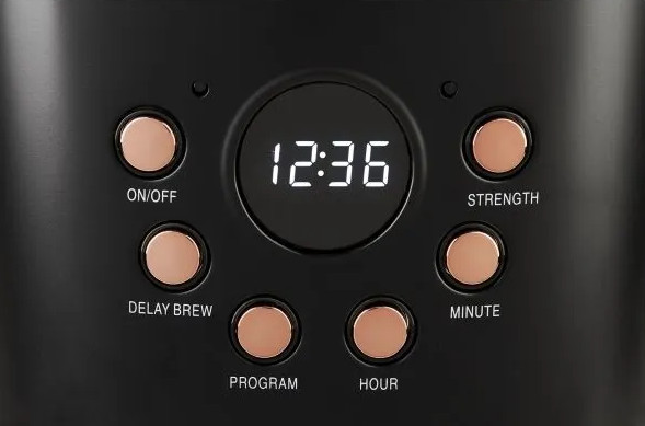 Zbliżenie panelu sterowania ekspresu do kawy. Wyświetlacz cyfrowy pokazuje czas. Kilka przycisków z etykietami.