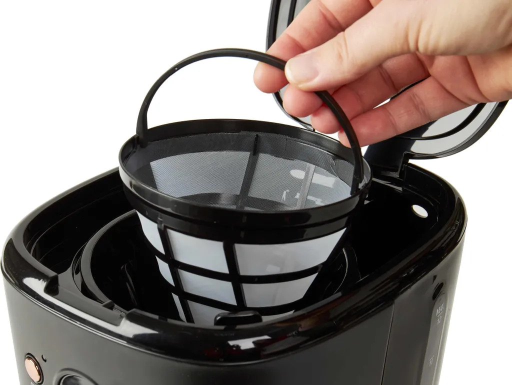 Ręka wkładająca filtr do kawy do ekspresu. Czarny ekspres, biały filtr. Zbliżenie.