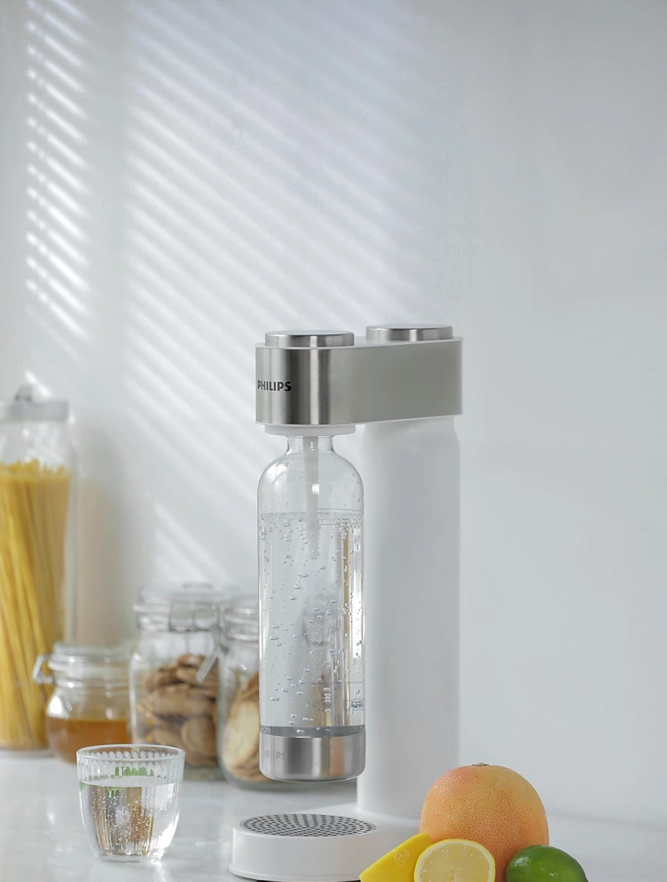 Urządzenie do produkcji sody ze szklaną butelką, innymi słoikami i owocami w kuchni ze światłem okiennym.