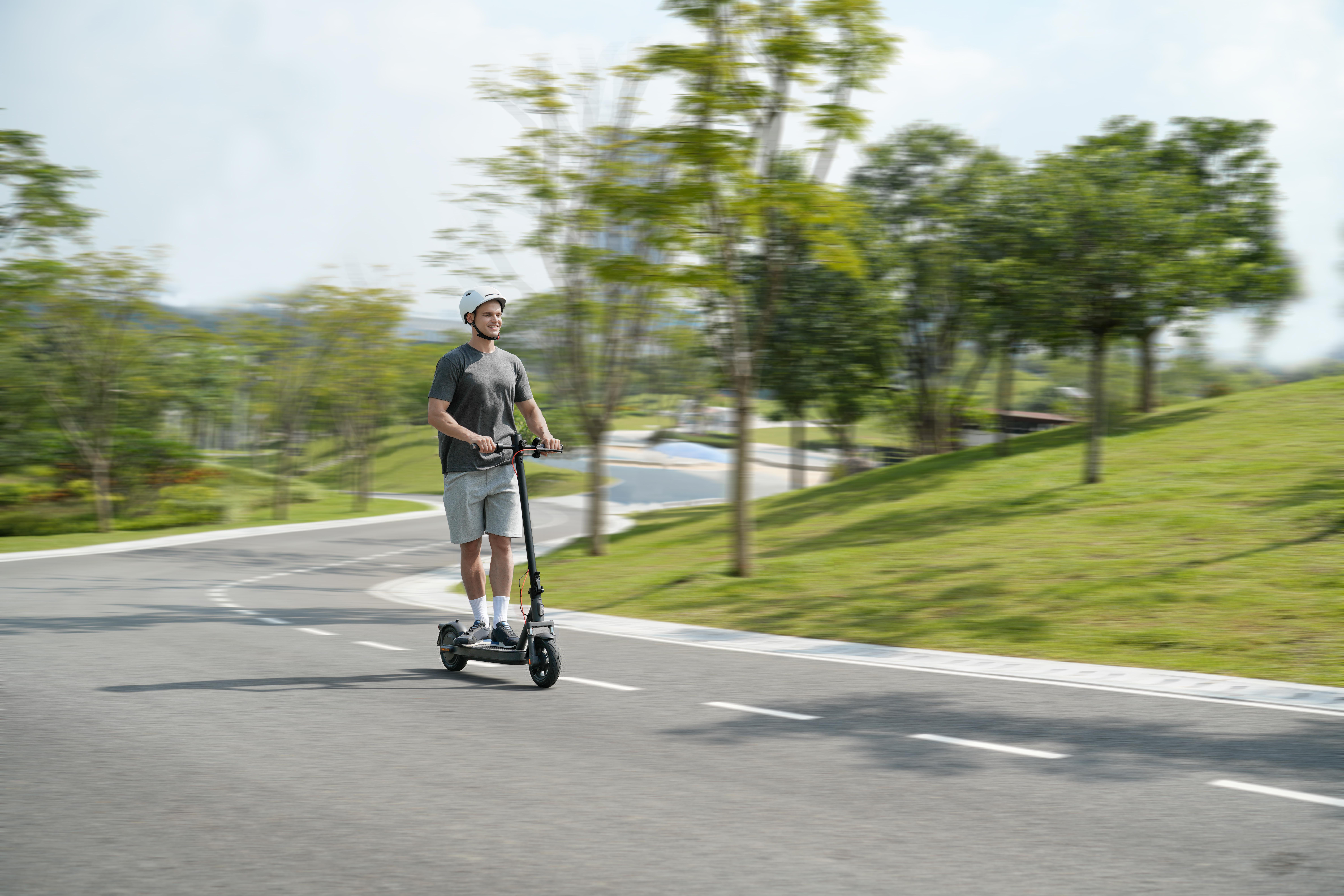 Ein Mann fährt mit einem Elektroroller auf einer Straße. Er trägt einen Helm und Shorts.