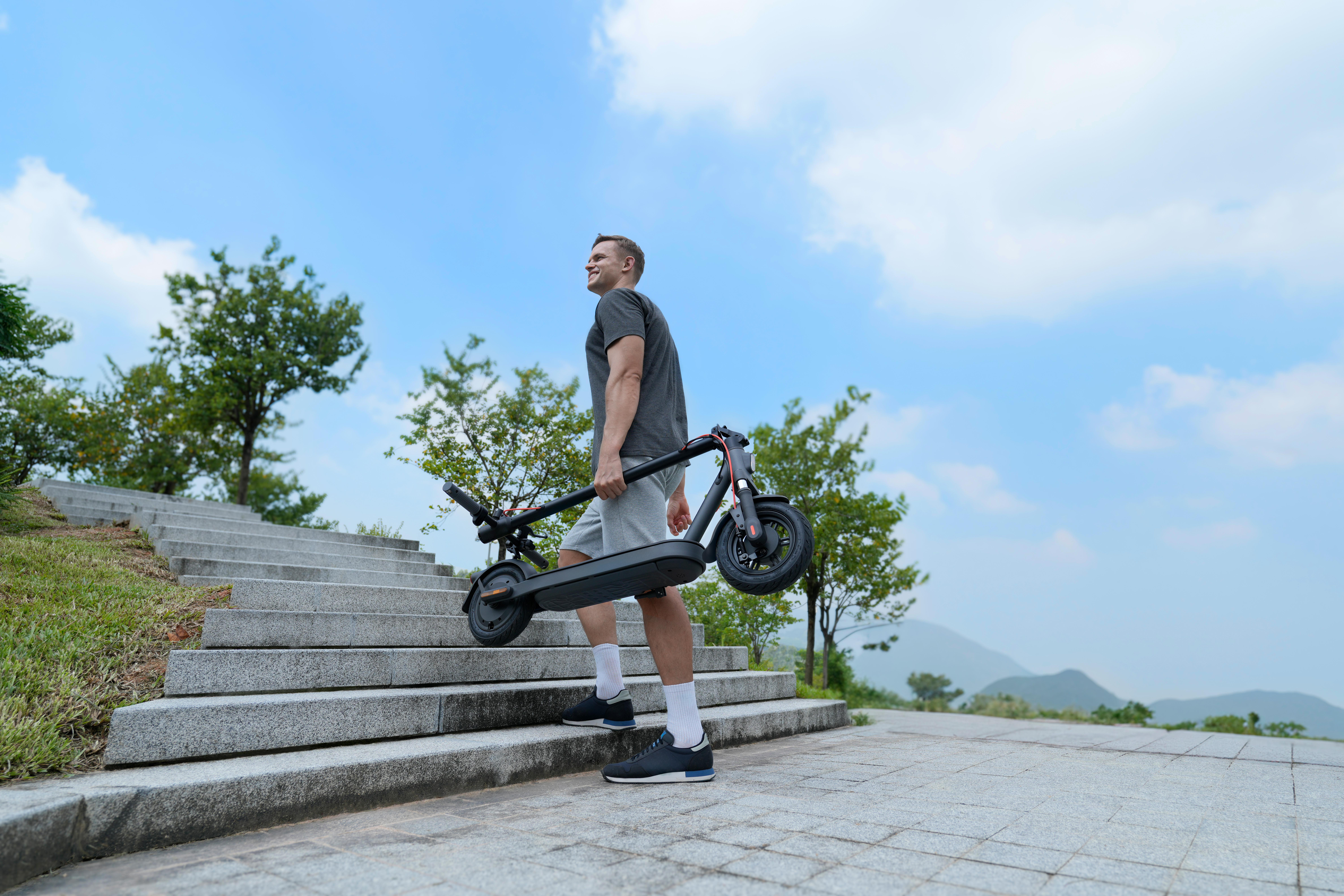 Ein Mann trägt einen Elektroroller die Treppe hoch. Er trägt Shorts und ein T-Shirt.