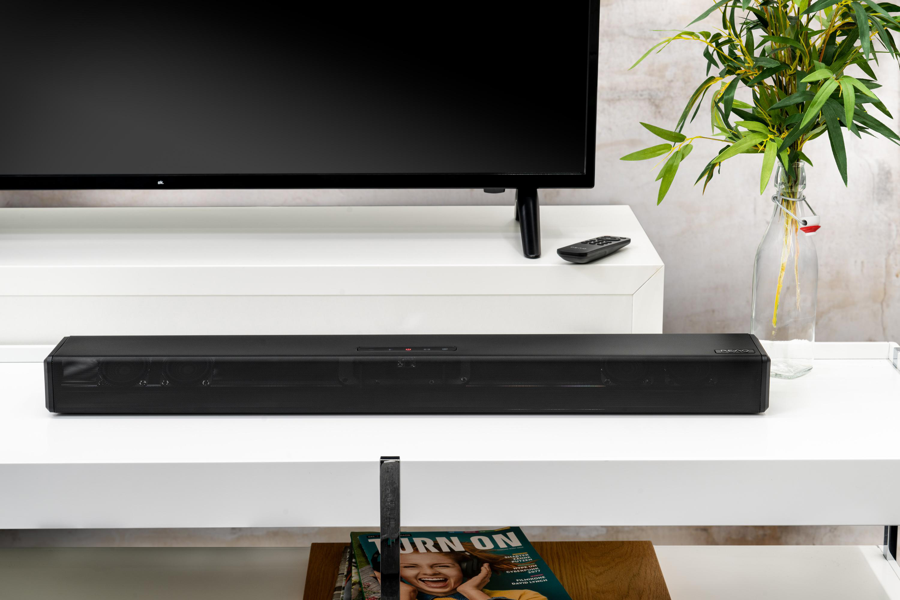 Eine schwarze Soundbar liegt auf einem weißen Regal unter einem Fernseher.
