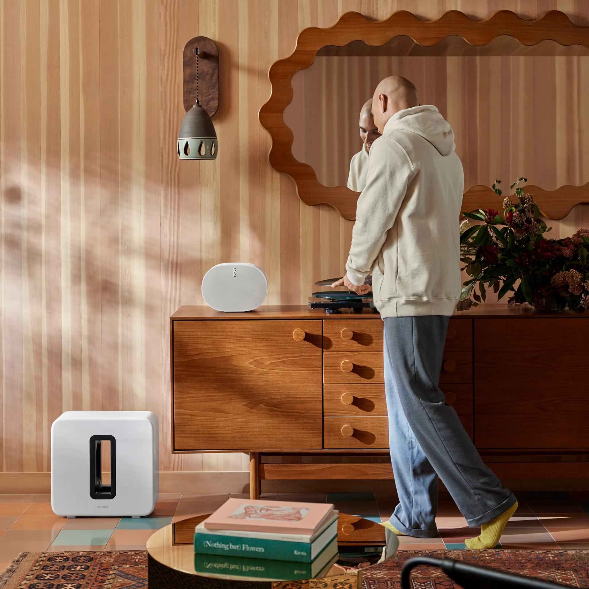 Scena w salonie z białym Sonos Sub i mężczyzną używającym gramofonu. Drewniane meble i dekoracje.