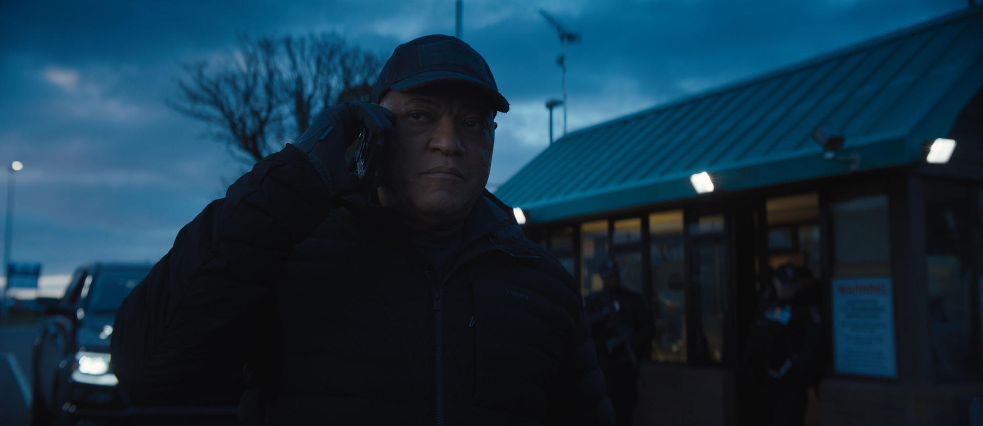 Laurence Fishburne telefoniert vor einem Gebäude. Dunkle Kleidung, Abenddämmerung.