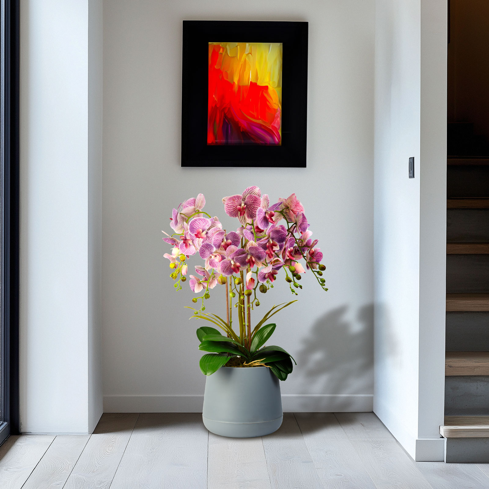 Rózsaszín orchidea szürke cserépben egy festmény mellett, egy ajtó előtt.