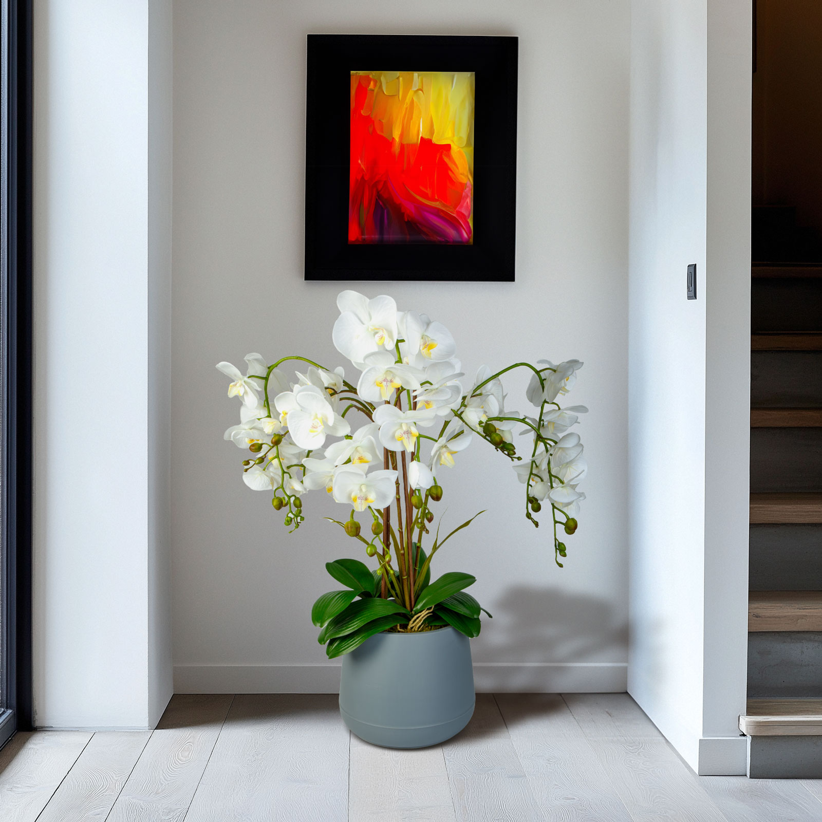 Fehér orchidea szürke cserépben egy festmény mellett, egy ajtó előtt.
