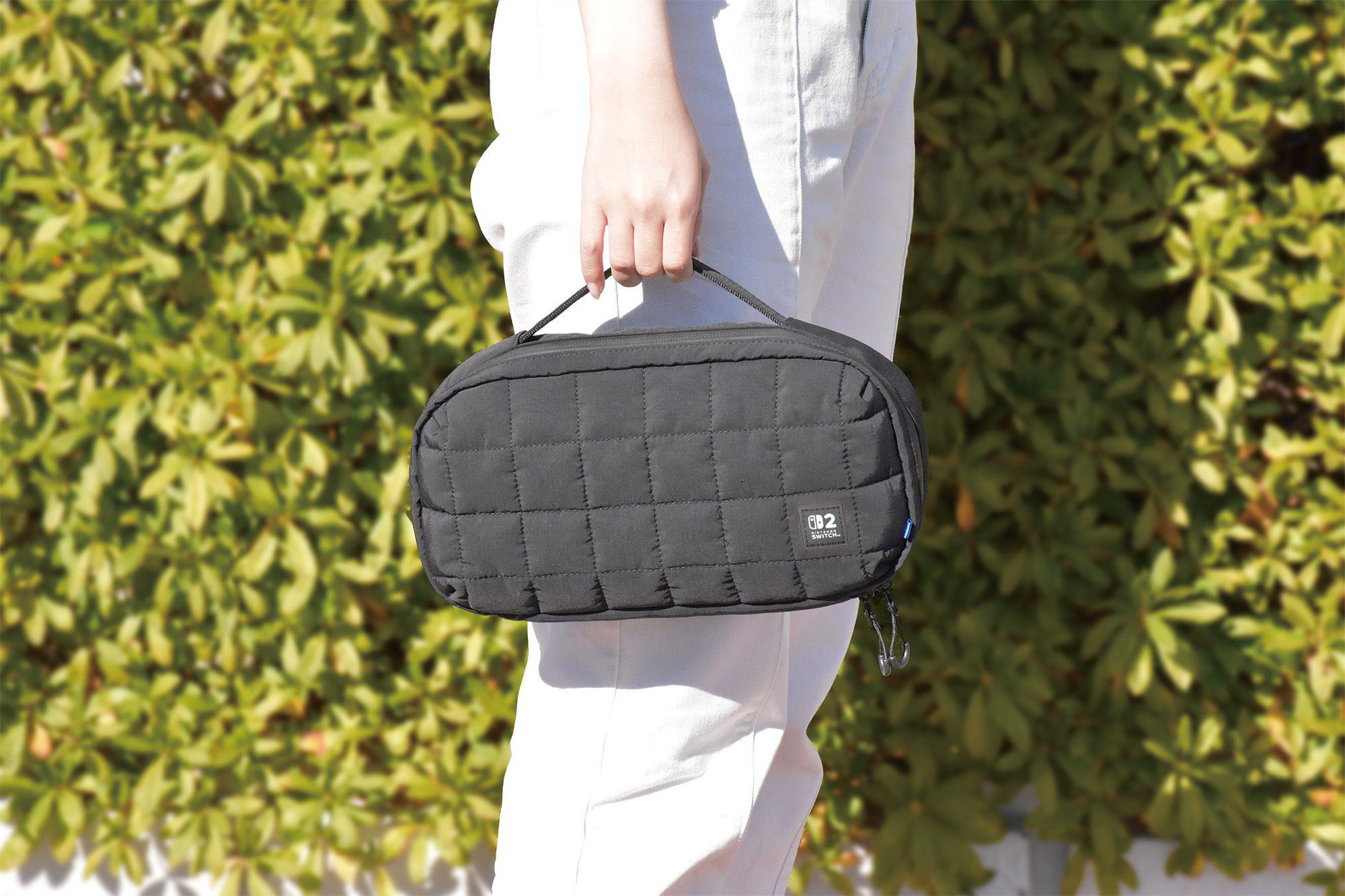 Eine Frau hält eine schwarze Tasche mit dem Nintendo Switch-Logo. Der Hintergrund ist grün.
