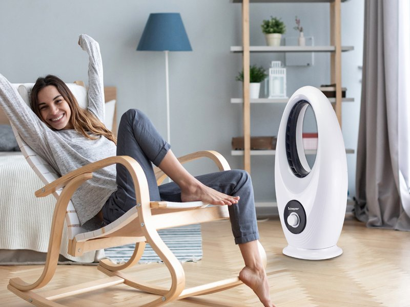 Nő élvezi a fehér ventilátort, miközben egy hintaszékben pihen.