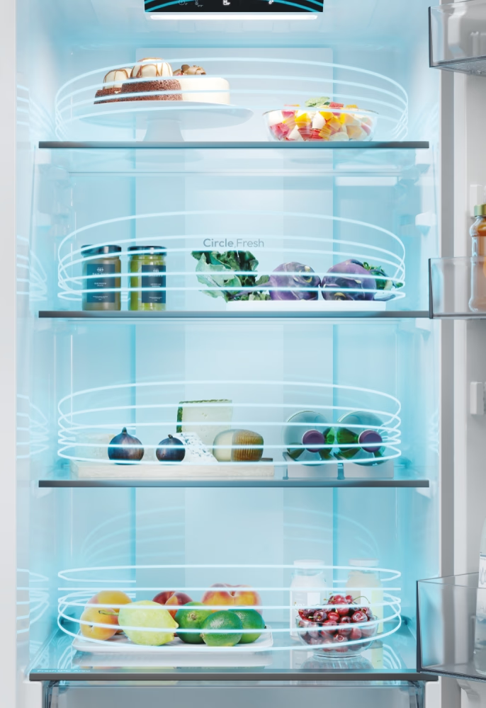 Intérieur du réfrigérateur avec aliments : bocaux, légumes, salade, gâteau. Étagères visibles.